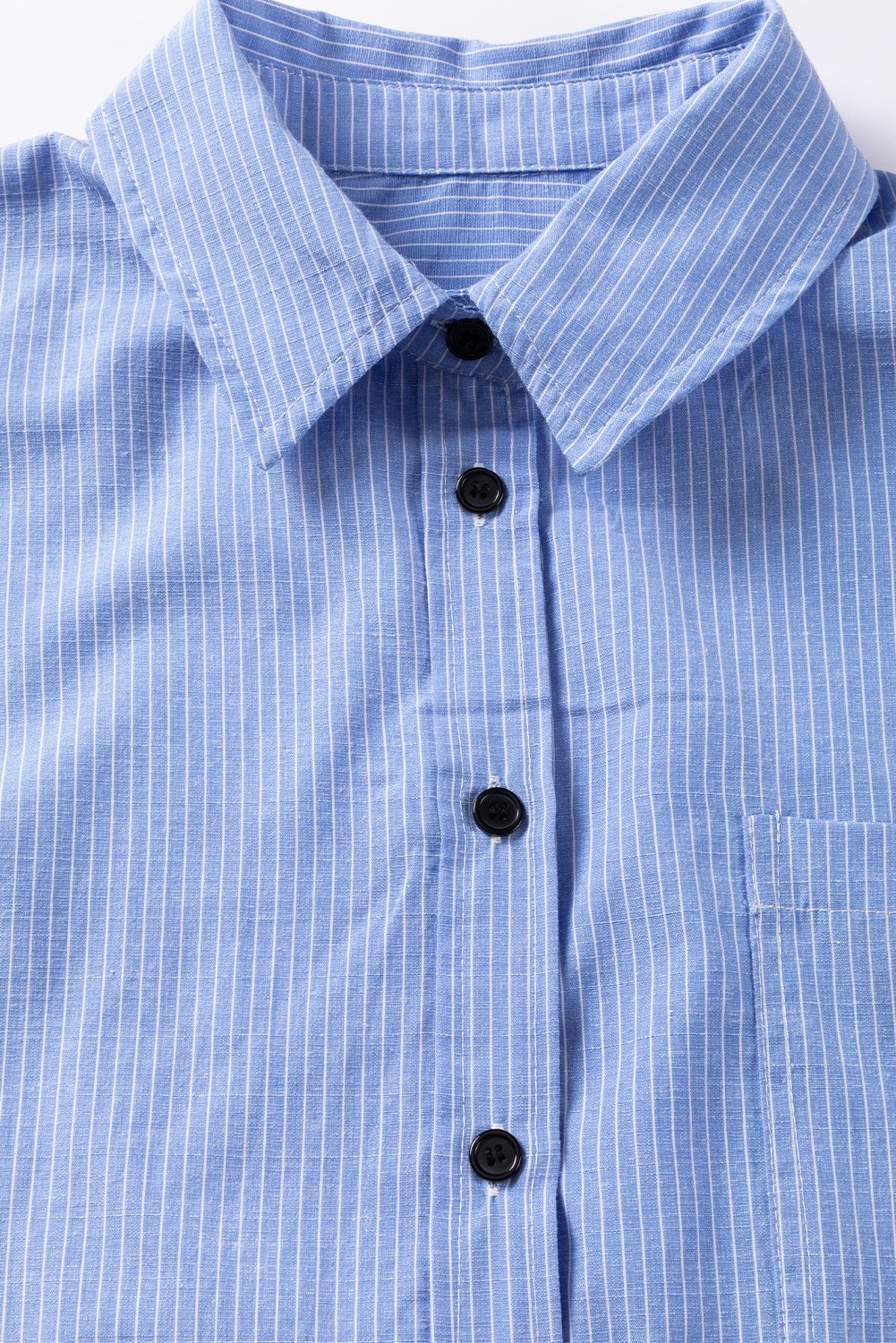 Close-up of sky blue long shirt with white stripes, roll-tab sleeves, black buttons, and chest pocket.