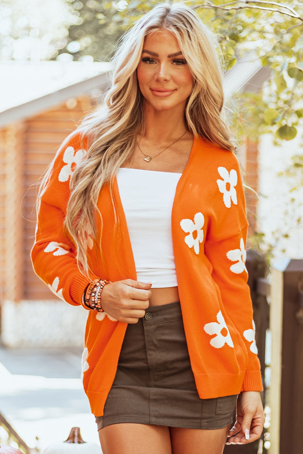 Orange floral print knitted open front loose cardigan worn over white top and olive skirt outdoors