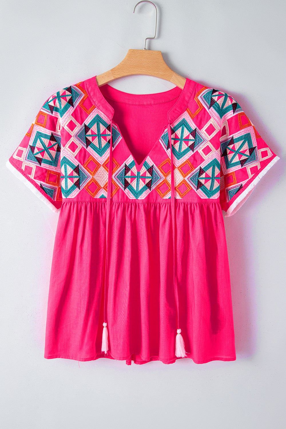 Bright colored summer blouse with embroidered tassel tie and geometric neck design.