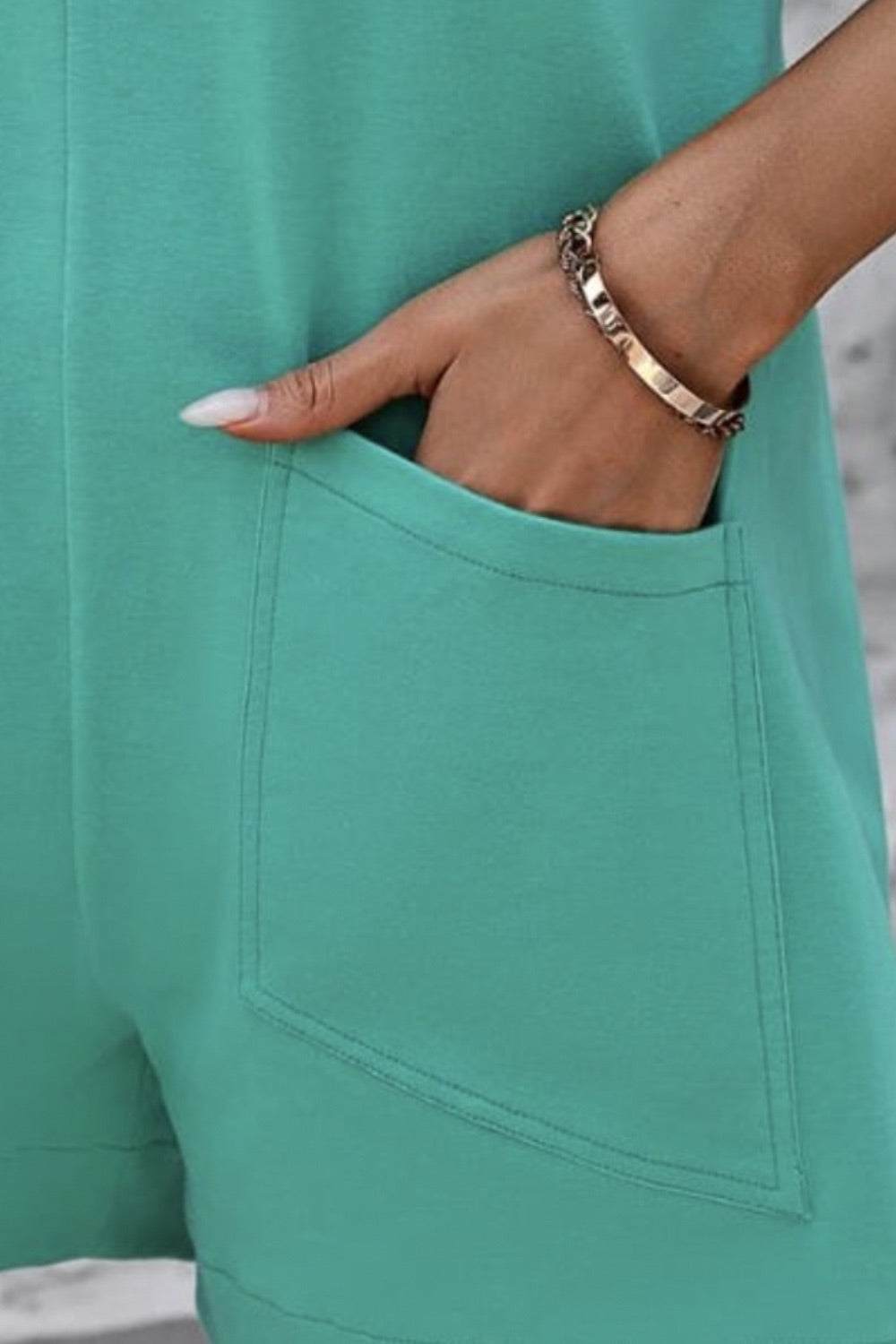 Sleeveless romper with round neck and front pocket in teal, featuring a relaxed fit.