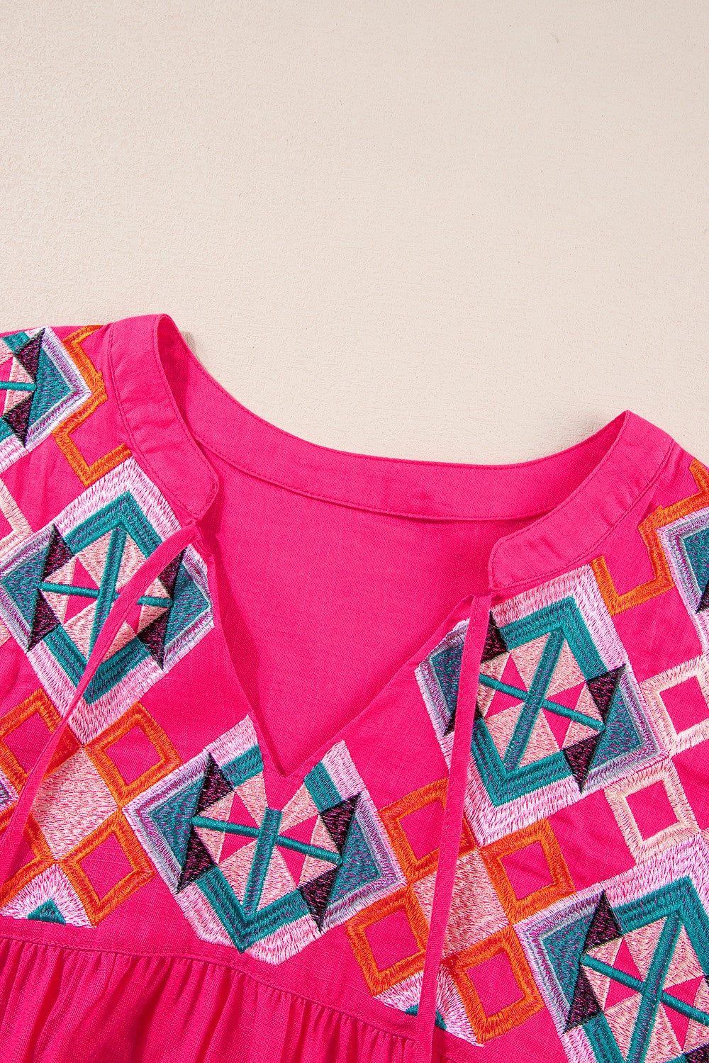 Bright pink blouse with embroidered geometric patterns and a tassel tie neckline.