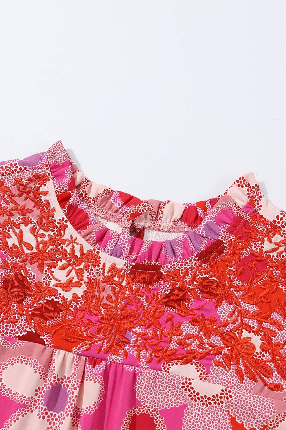 Floral ruffled cap sleeve blouse with red embroidered details on neckline and sleeves.