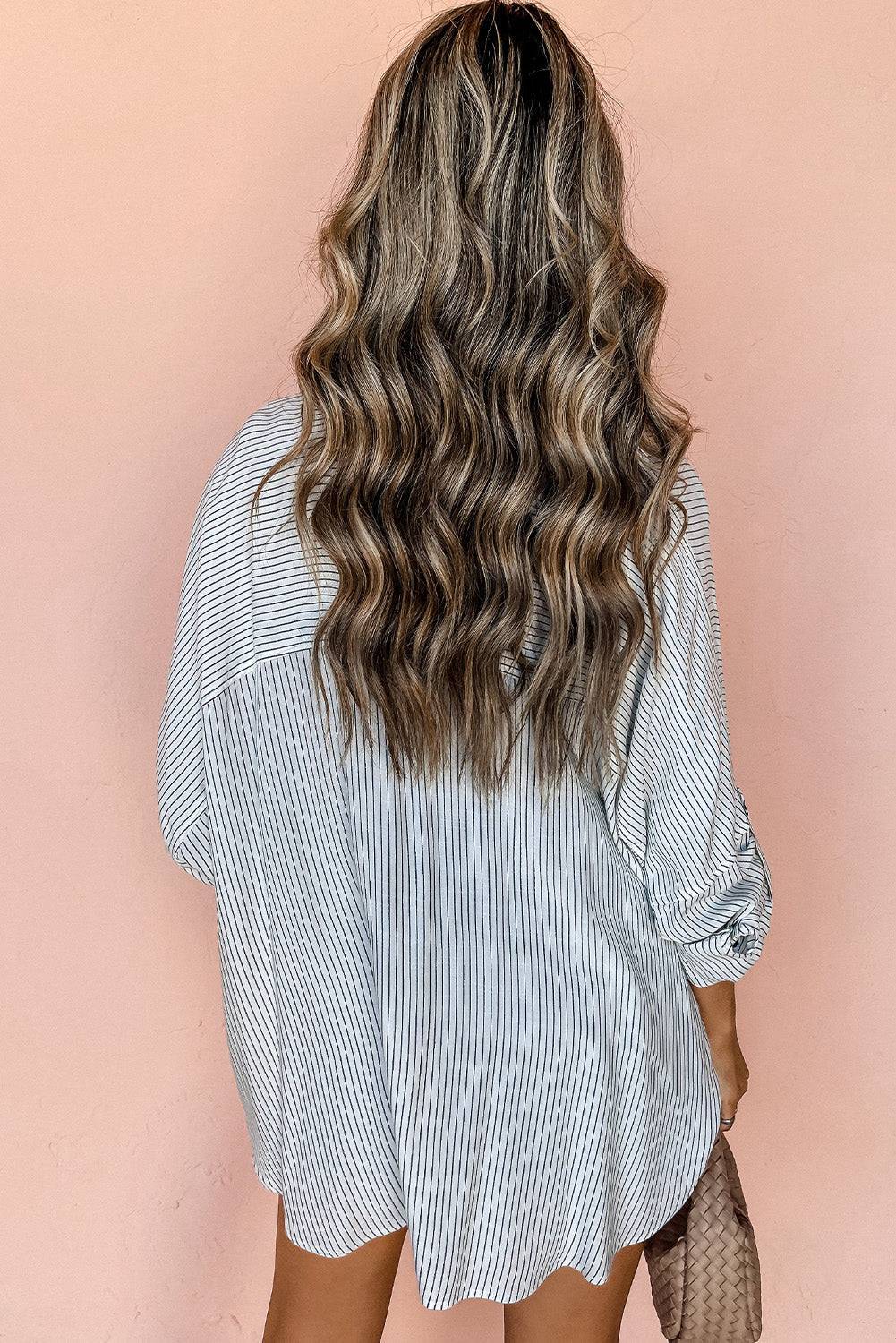 Woman wearing DEAR-LOVER striped roll-tab sleeve pocketed long shirt viewed from back against peach background