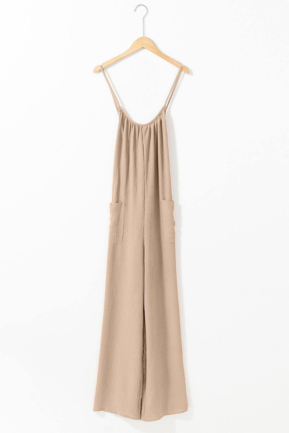 Apricot wide leg jumpsuit with spaghetti straps, waist tie, and side pockets hanging on wooden hanger against white background