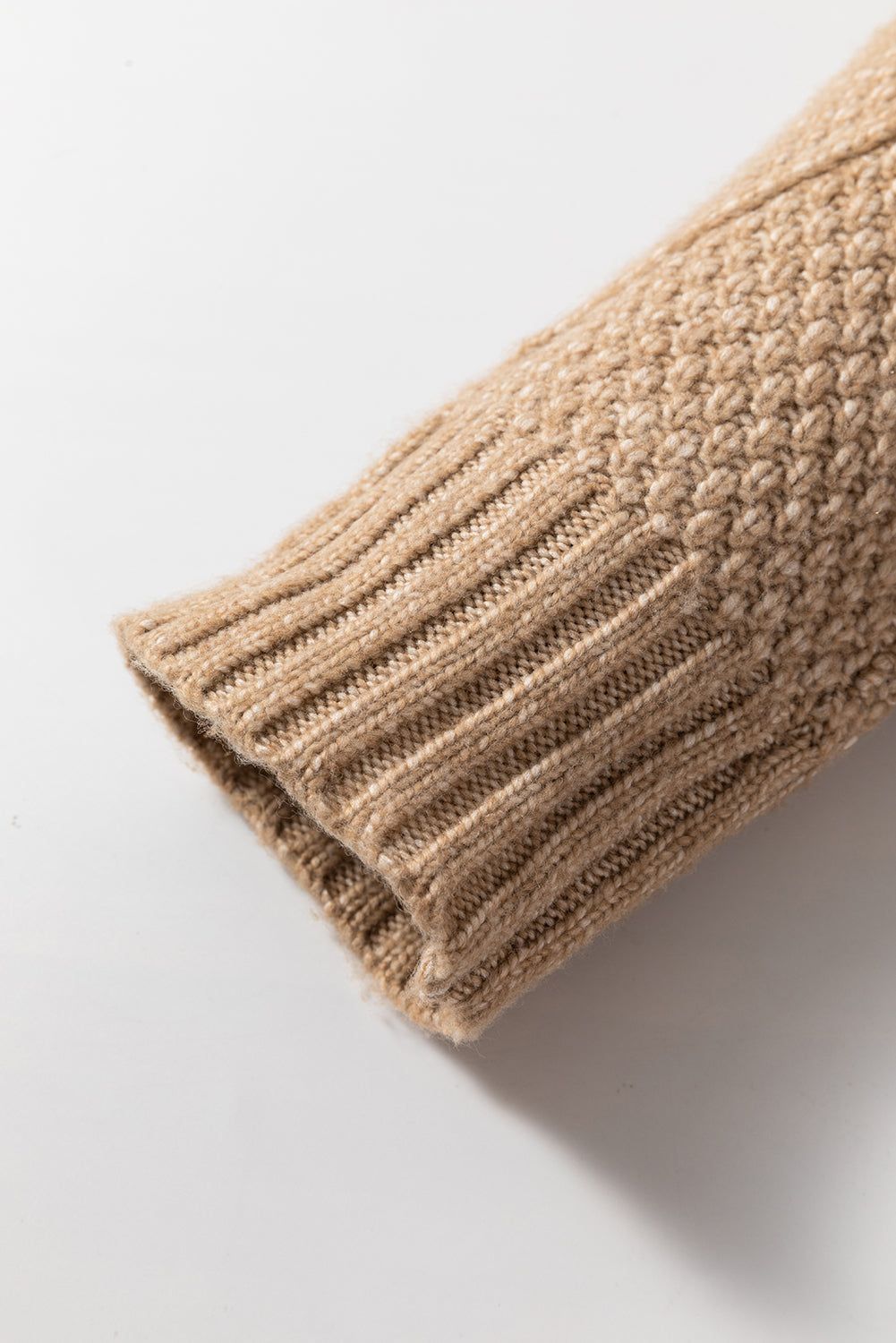 Close-up of sleeve on a beige cable knit sweater dress, featuring ribbed cuffs and intricate knit texture.