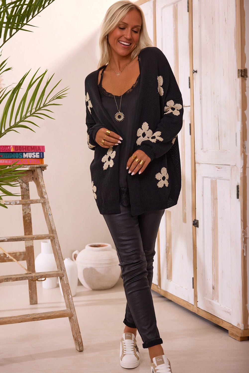 Woman wearing black floral print knitted open front loose cardigan with leather pants and white sneakers indoors