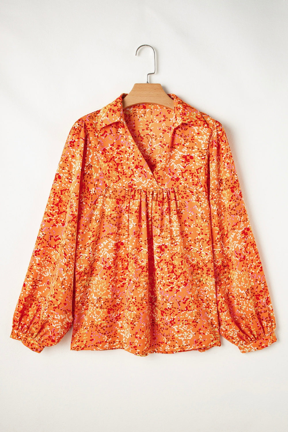 Orange abstract print collared V-neck babydoll blouse hanging on a hanger.