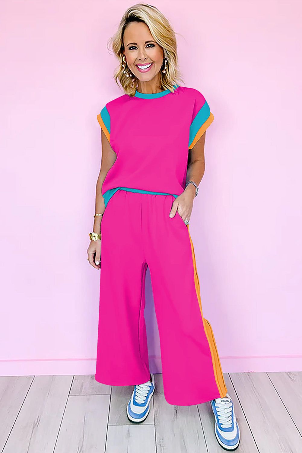 Woman wearing strawberry pink color block casual two-piece set with blue and orange accents and white sneakers against pink background
