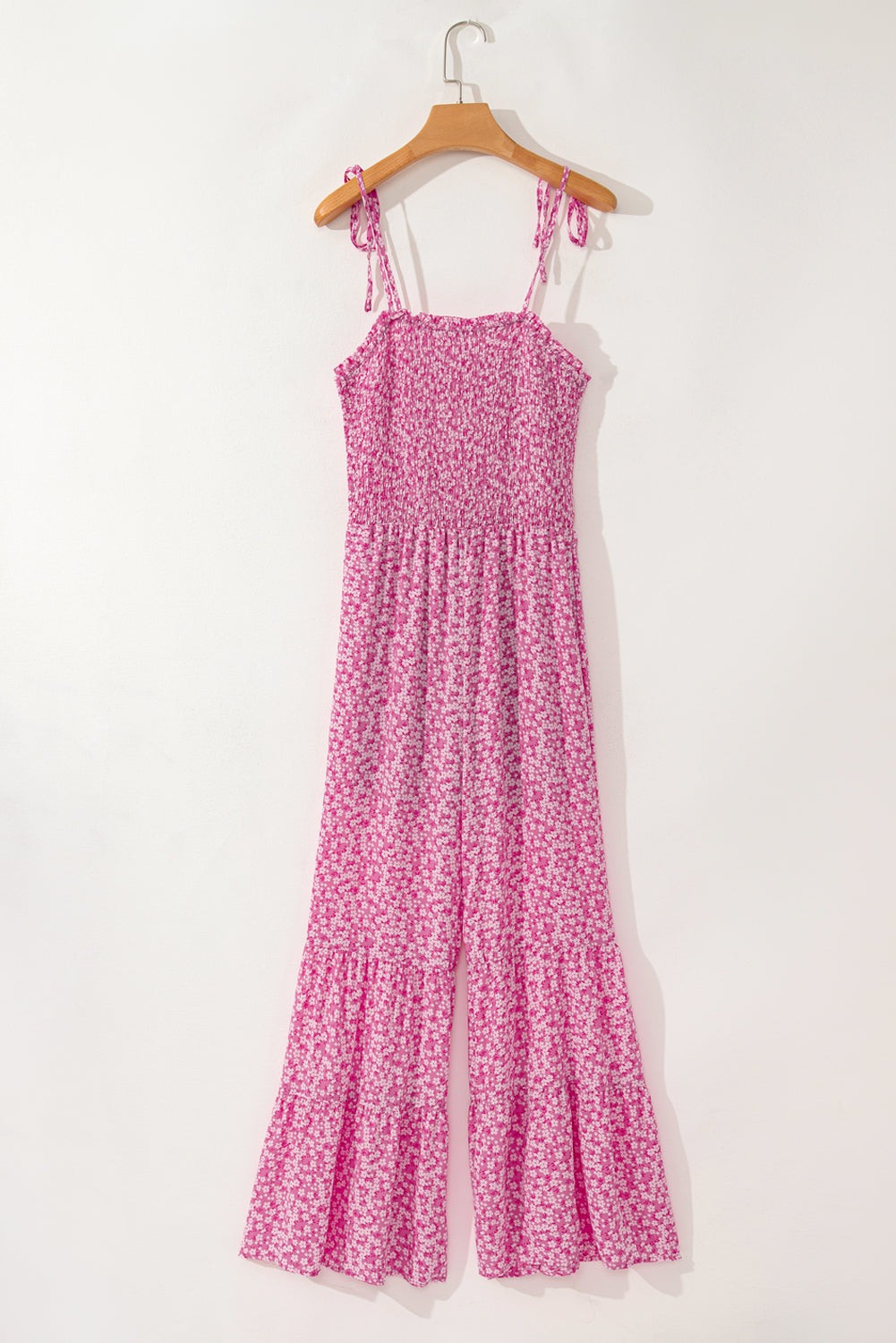 Pink floral Phalaenopsis wide leg jumpsuit with smocked bodice and adjustable thin straps hanging on wooden hanger