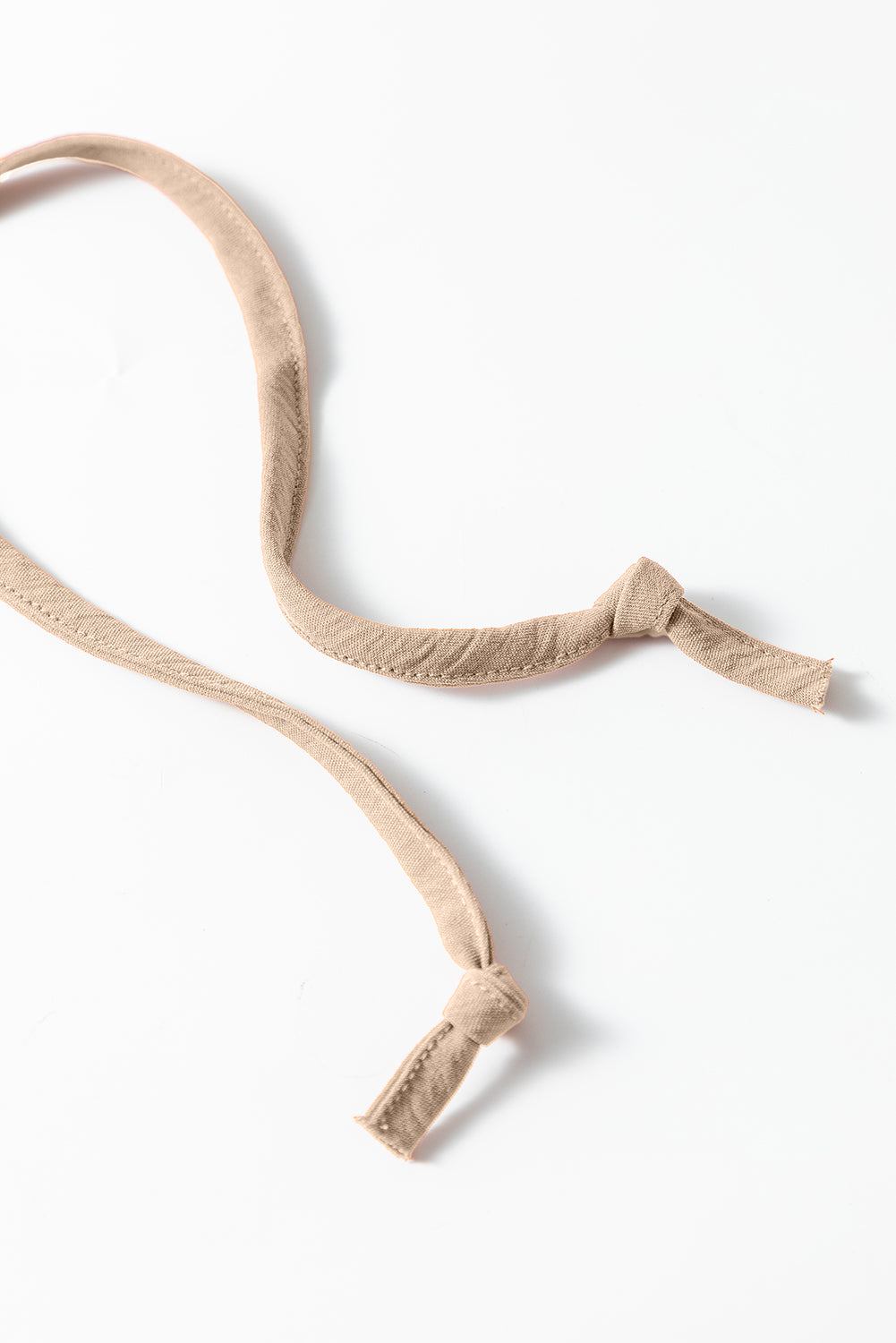 Close-up of apricot-colored spaghetti strap ties from a wide leg jumpsuit with waist tie and pockets