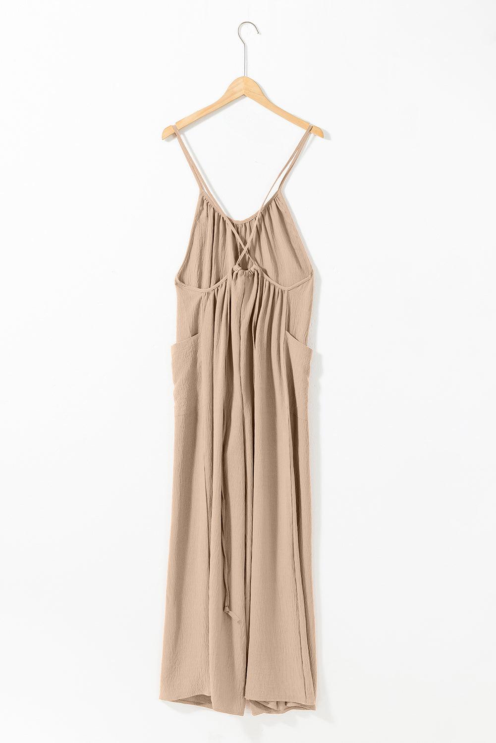 Apricot wide leg jumpsuit with spaghetti straps, waist tie, and side pockets hanging on wooden hanger.