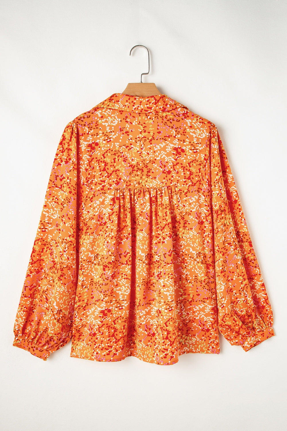 Orange abstract print babydoll blouse with collared V-neck and relaxed fit hanging on a wooden hanger.