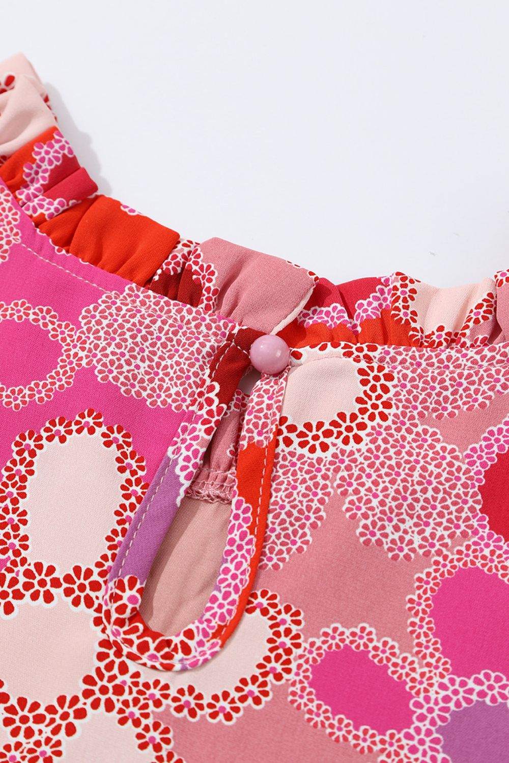 Floral ruffled cap sleeve blouse with embroidered detail and button closure.