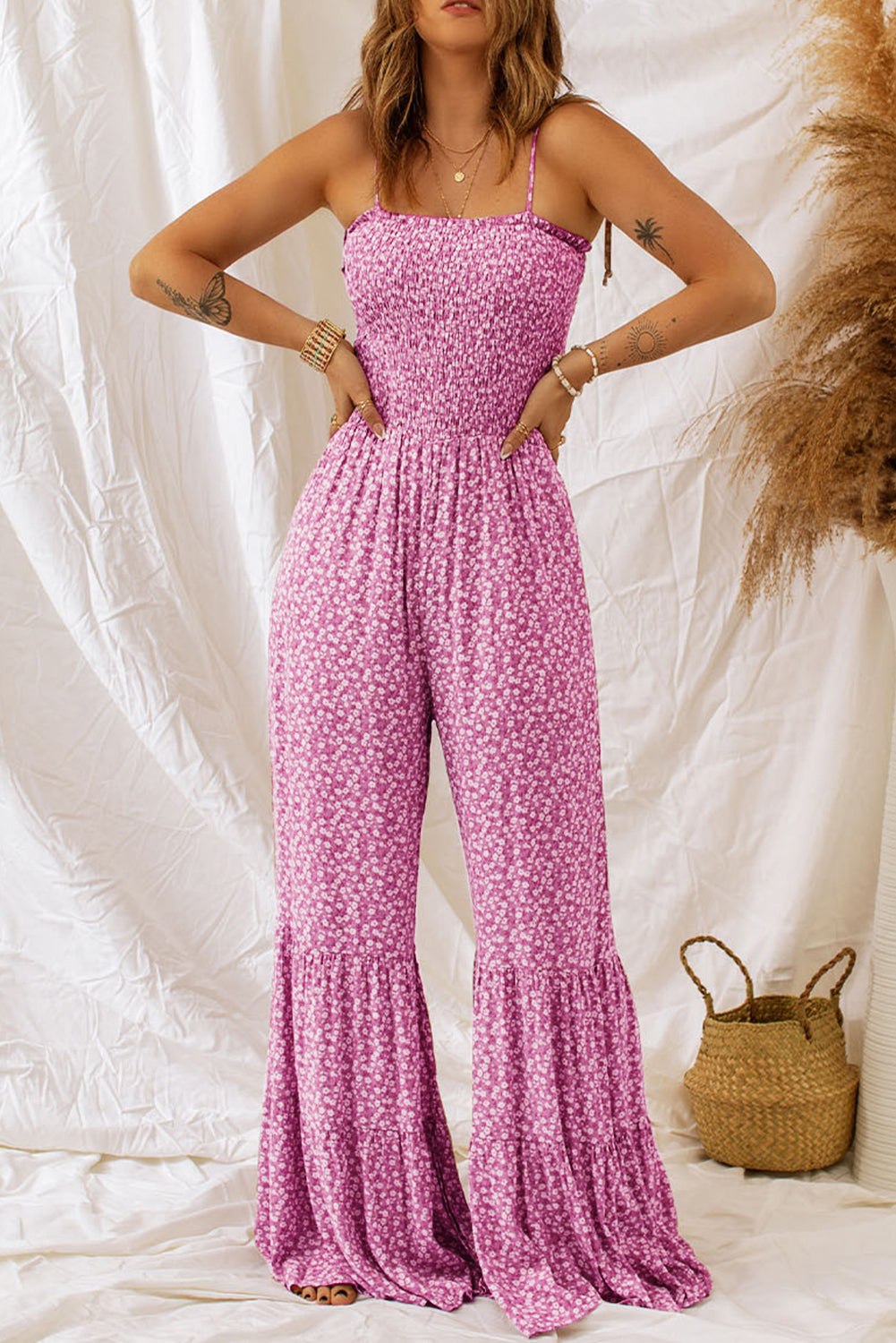 Woman wearing a pink floral smocked bodice wide leg jumpsuit with thin straps standing indoors