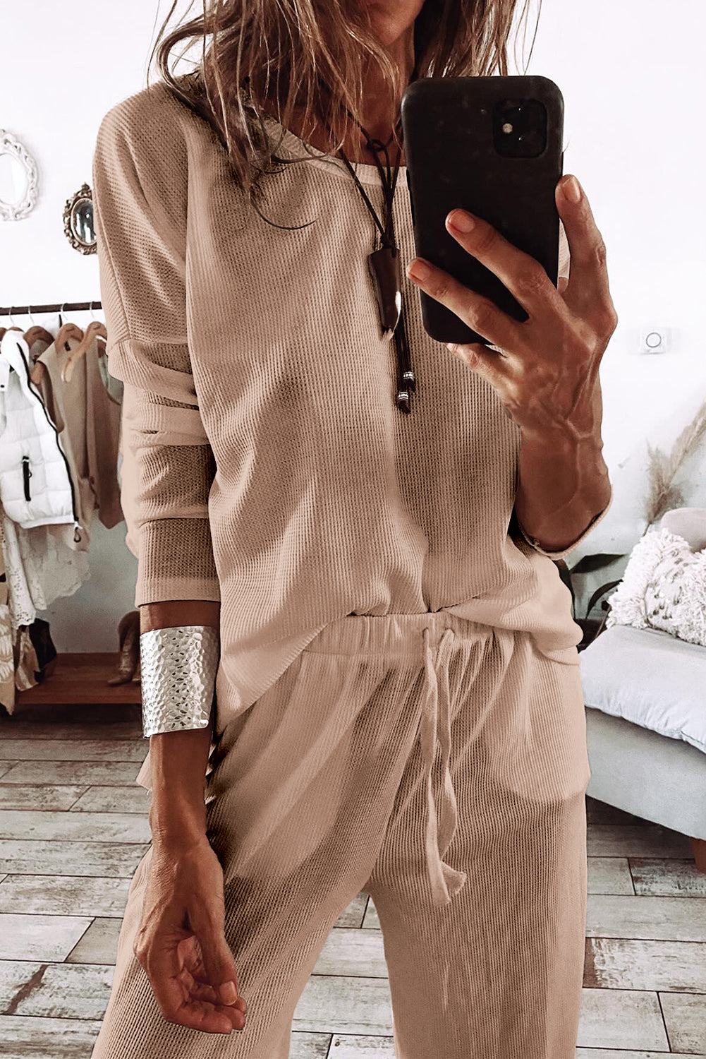 Woman wearing beige parchment textured lounge set with drawstring pants taking mirror selfie in stylish room