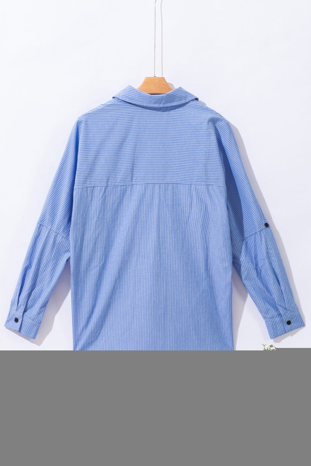 Sky blue striped long shirt with roll-tab sleeves and chest pocket hanging on wooden hanger, back view