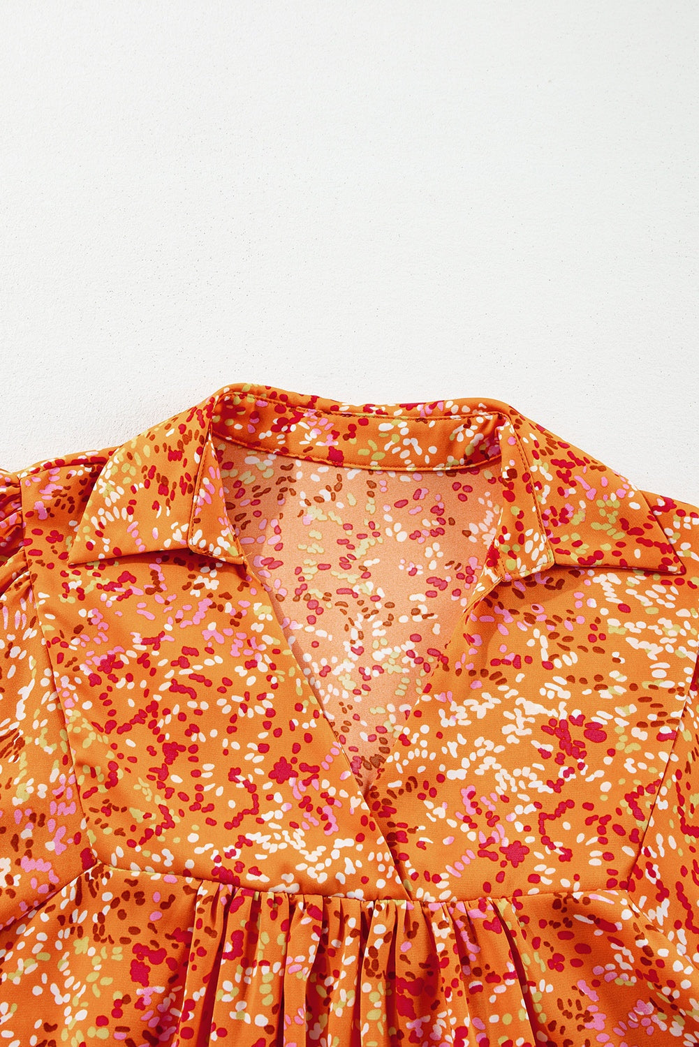 Orange abstract print collared V-neck babydoll blouse with playful design.
