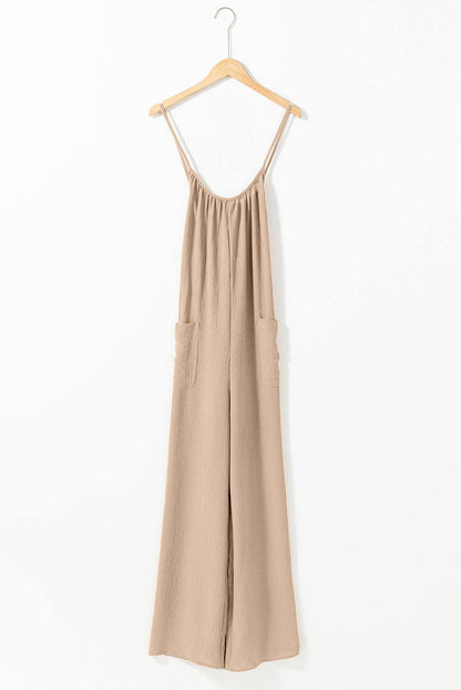 Apricot wide leg jumpsuit with spaghetti straps, waist tie, and side pockets hanging on wooden hanger against white background