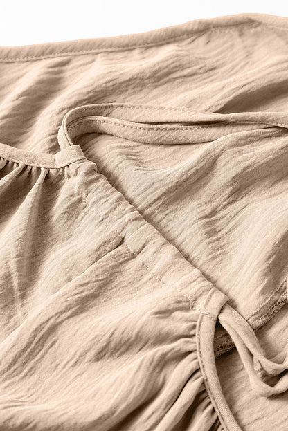 Close-up of apricot wide-leg jumpsuit fabric with spaghetti straps and waist tie detail