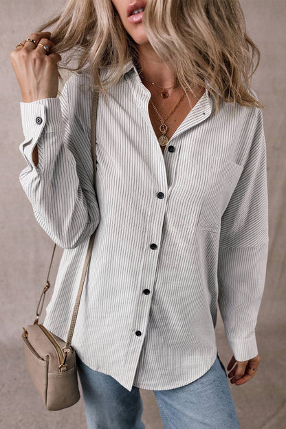 Woman wearing DEAR-LOVER striped roll-tab sleeve pocketed long shirt with buttons, paired with jeans and a beige shoulder bag