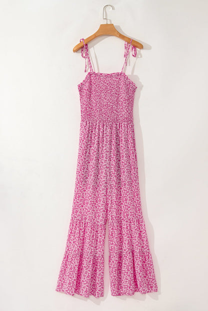 Pink floral Phalaenopsis wide leg jumpsuit with smocked bodice and adjustable thin straps hanging on wooden hanger