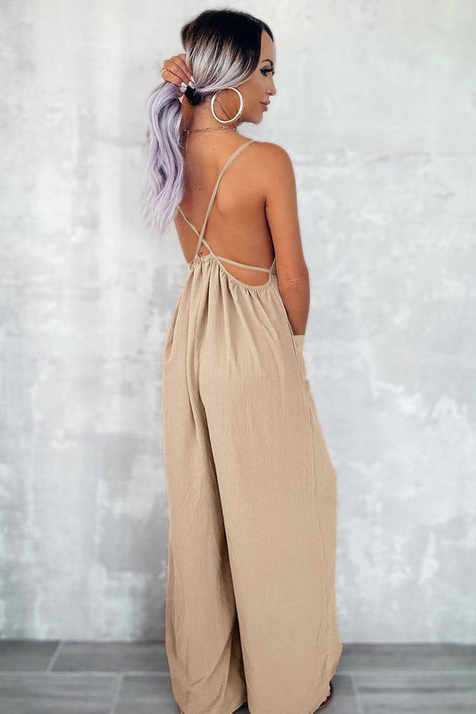 Woman wearing apricot spaghetti strap wide leg jumpsuit with waist tie and pockets, back view