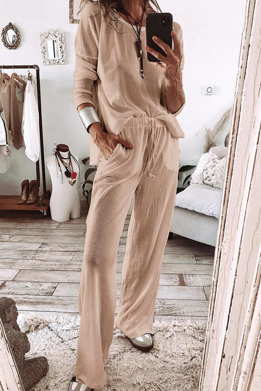 Woman wearing beige parchment textured lounge set with relaxed fit top and tapered pants in cozy modern room with mirror and casual decor