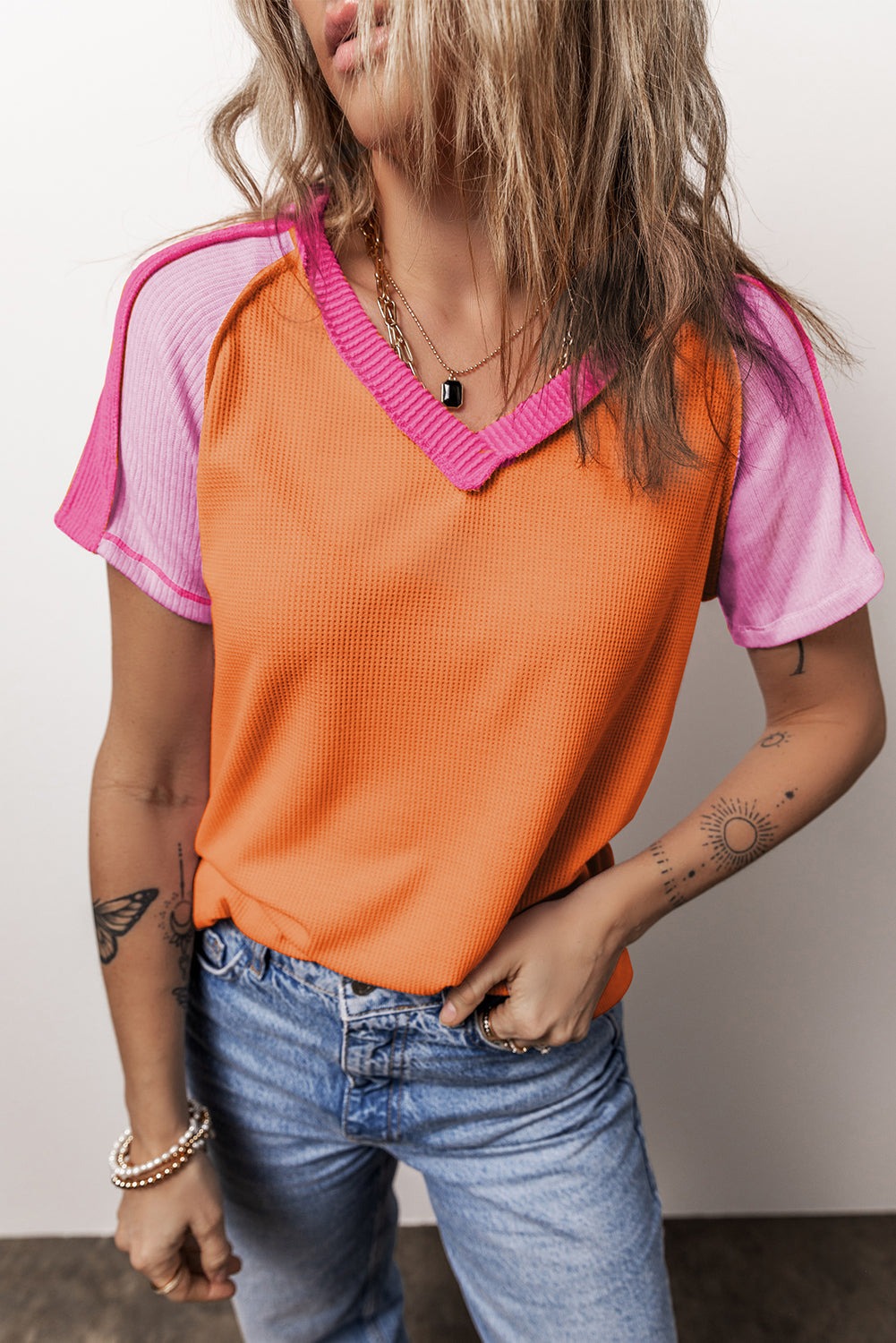 Woman wearing orange and pink color block V-neck knitted T-shirt with exposed seams and blue jeans