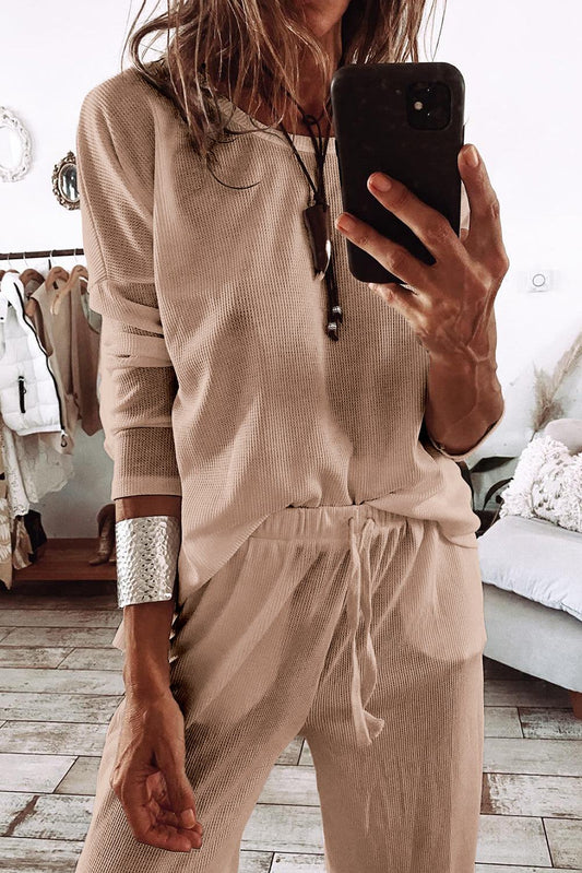Woman wearing beige parchment textured lounge set with drawstring pants taking mirror selfie in stylish room