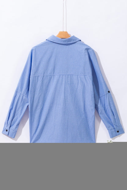 Sky blue striped long shirt with roll-tab sleeves and chest pocket hanging on wooden hanger, back view